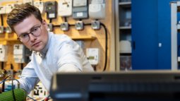 An electrical engineering student works in a lab with various components and equipment, focusing on a hands-on technical task.