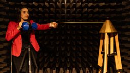 An Electrical Engineering student stands in an anechoic chamber, testing her project work.