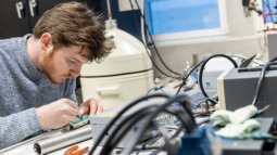 A Biomedical Signals and Systems student works on an electronic circuit in a lab filled with specialised equipment and cables.