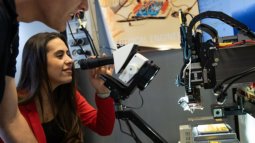Electrical Engineering student uses a microscope while another observes, surrounded by lab equipment and a computer monitor.