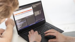 Two Computer Science students work on a laptop displaying code and data analysis.