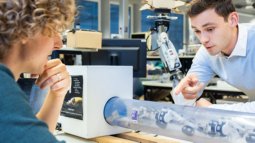 Students discuss a robotic arm in a transparent tube in the RAM lab at the University of Twente.