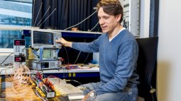 A teacher operates electronic testing equipment in a lab, surrounded by connected devices and wires on the table.