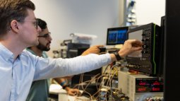 Two students work with electronic equipment and an oscilloscope, monitoring data on screens in a technical lab.